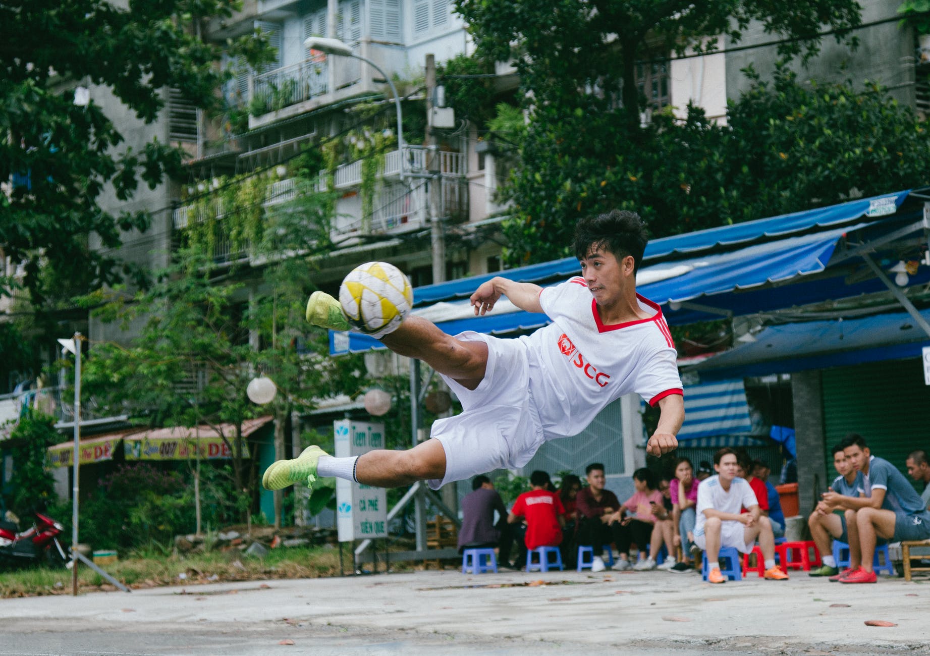 soccer player kick the ball near people sitting on canopy tent
