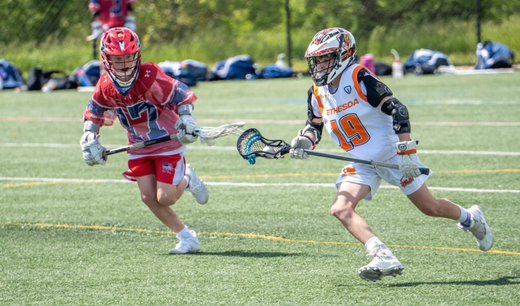 young athletes running on the field while holding a lacrosse stick